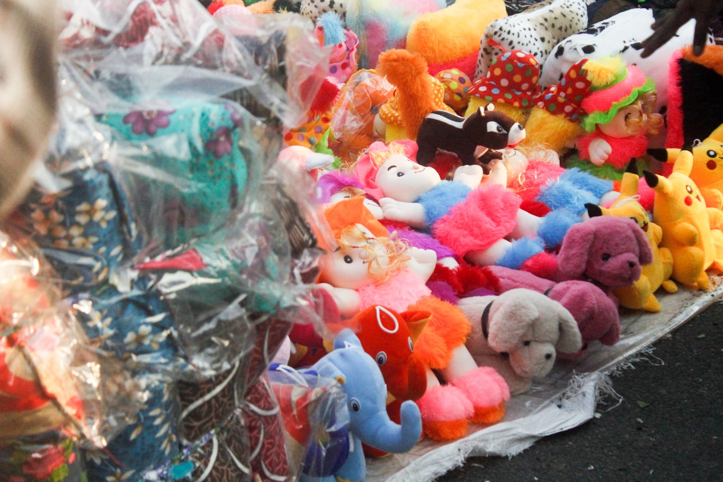A hand touches stuffed toys displayed at a market stall.